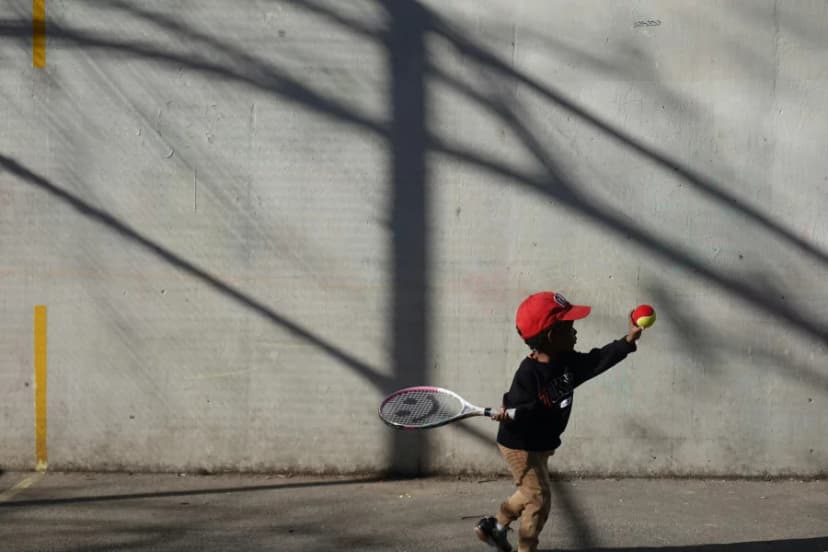 Young child playing tennis against a wall